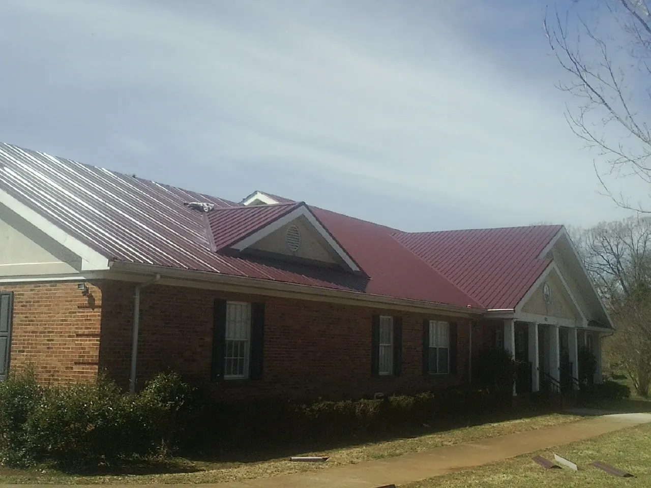 Red metal roof with gabled entries on a long brick building, from a Hail Damage Roof Repair job in Coventry