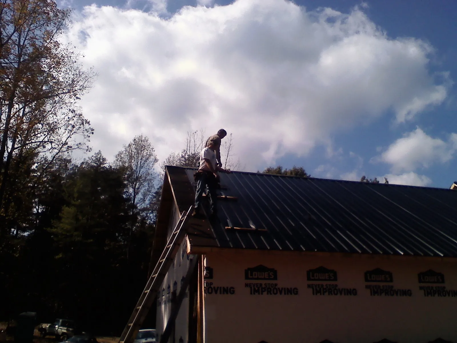 Roofer fastening dark metal panels high against a cloudy sky, from a Roof Inspection job in Coventry